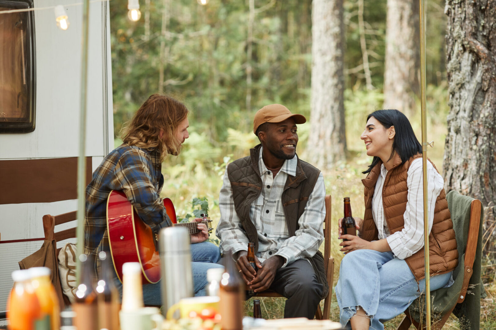 Group of three friends enjoying camping outdoors with trailer van and drinking beer